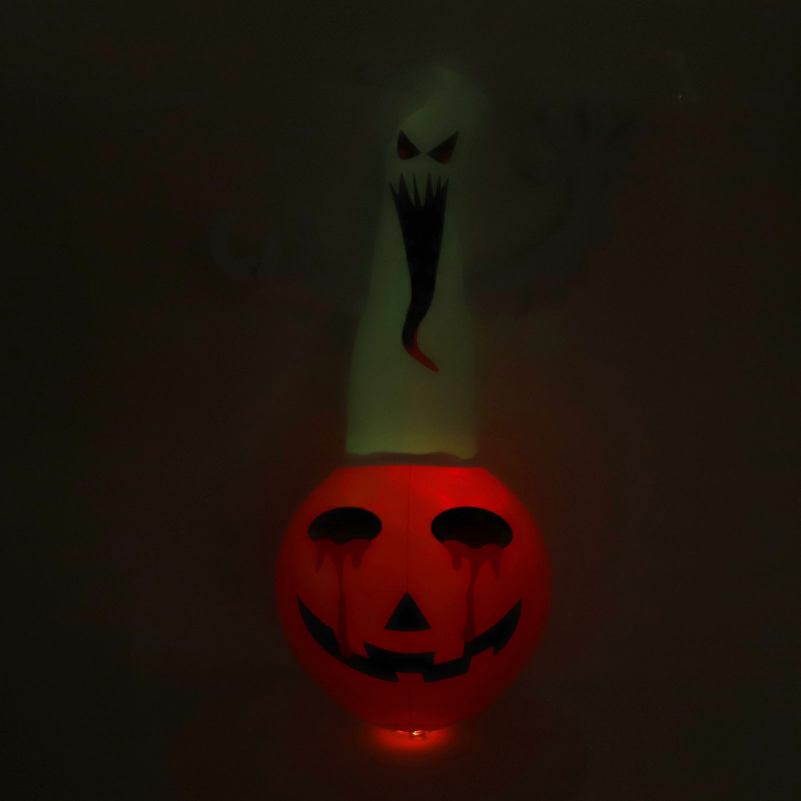 Leuchtende Halloween-Dekoration mit Kürbis und Geist. Der Kürbis hat ein gruseliges Gesicht mit Tränen. Dunkler Hintergrund.