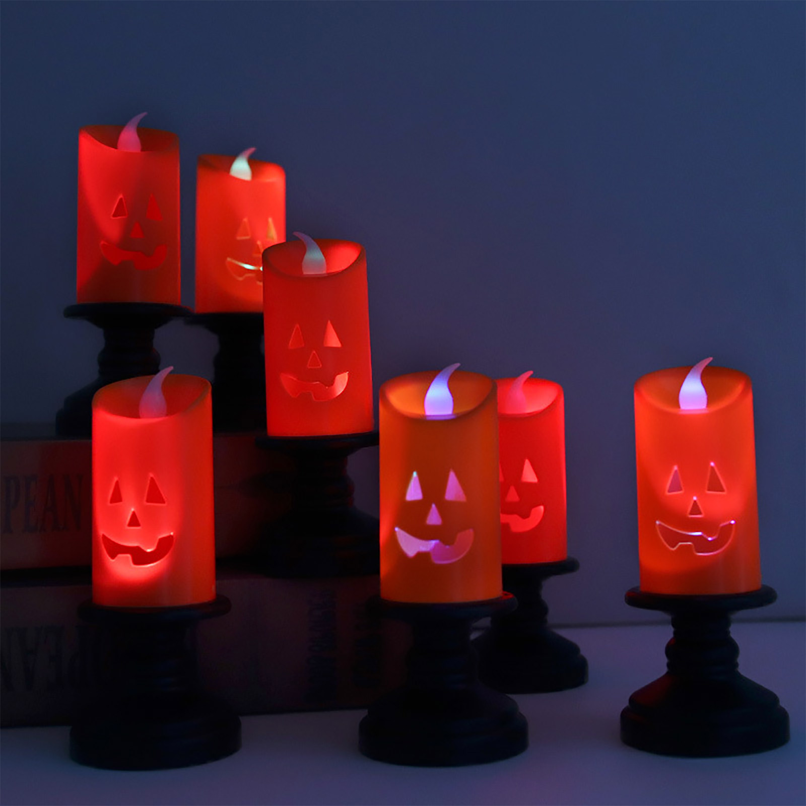 Mehrere brennende orangefarbene Kürbiskerzen auf schwarzen Ständern, eine Halloween-Dekoration, auf einer weißen Oberfläche, vor blauem Hintergrund.