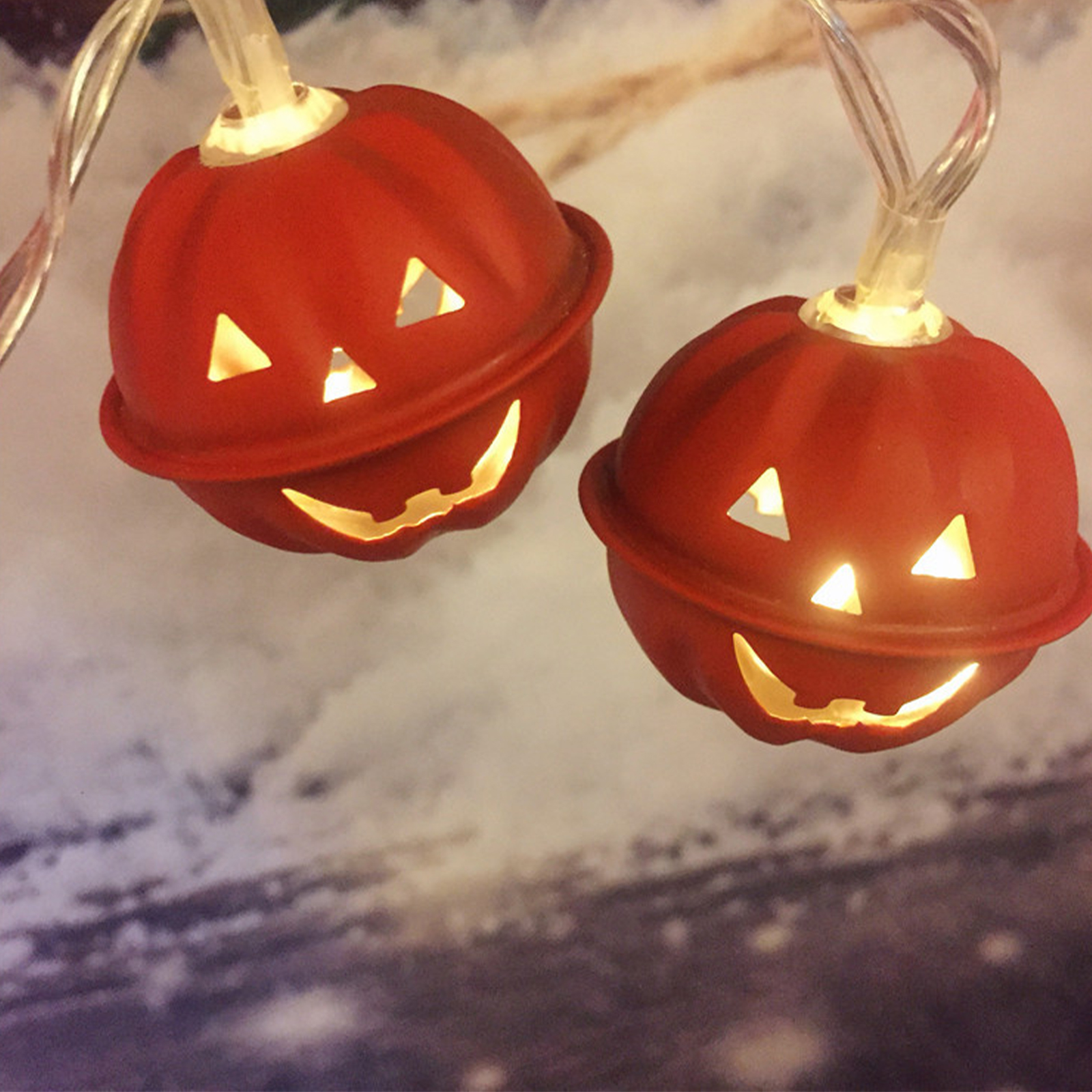 Zwei rote Halloween-Kürbislichter mit dreieckigen Augen und lächelnden Mündern, die leuchten. Der Hintergrund ist verschwommen, mit Weiß und Braun.