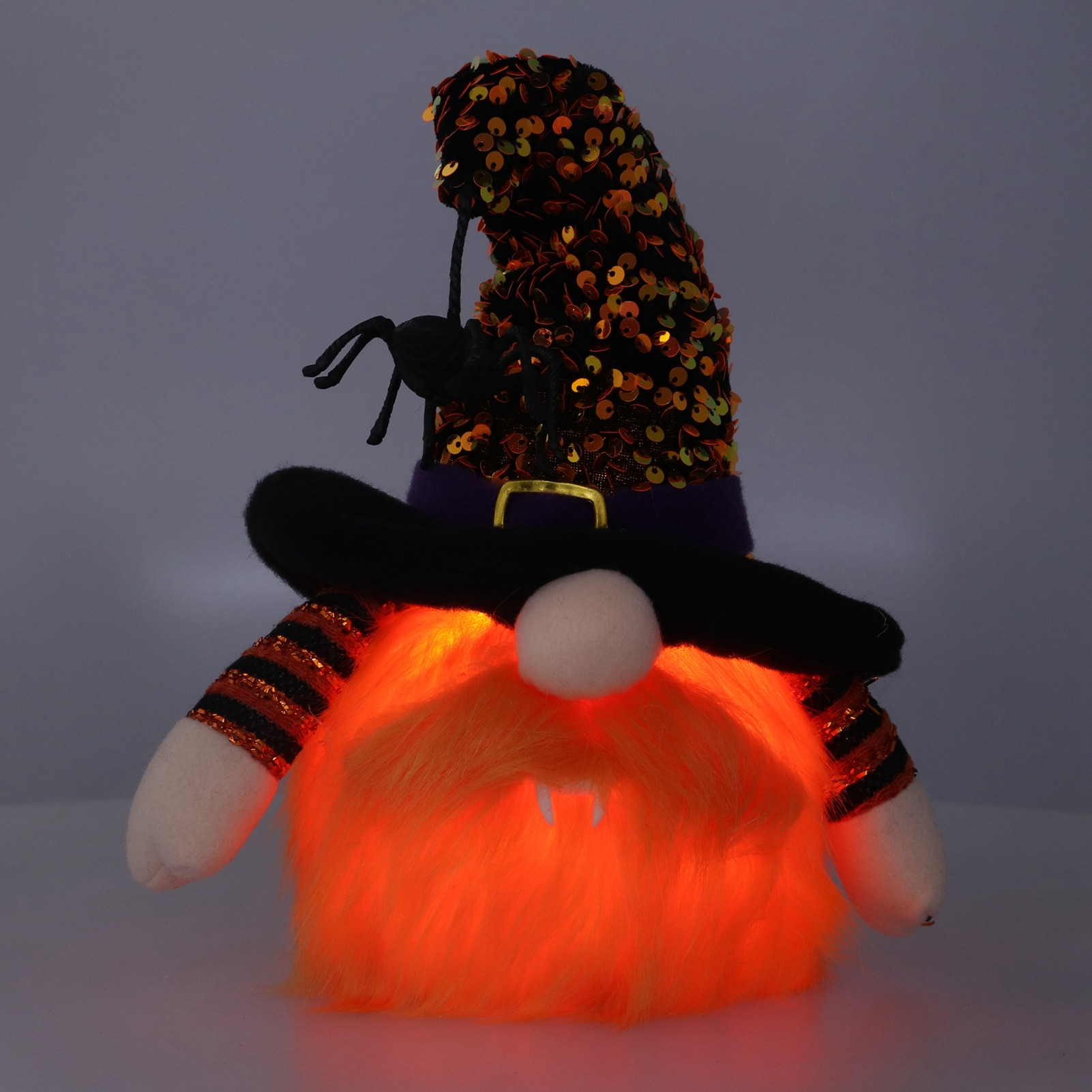 Ein Halloween-Zwerg mit schwarzem Hut, Spinne, orangefarbenem Bart und leuchtend orangefarbenem Fell. Er hat gestreifte Ärmel.