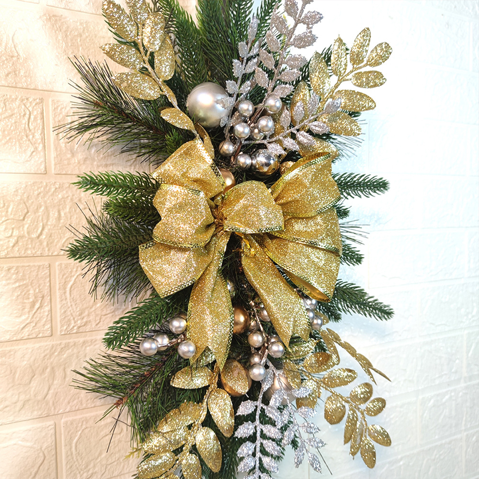 Ein festliches Arrangement aus Kiefer, goldenen Glitzerblättern, silbernen Beeren und einer großen goldenen Schleife.