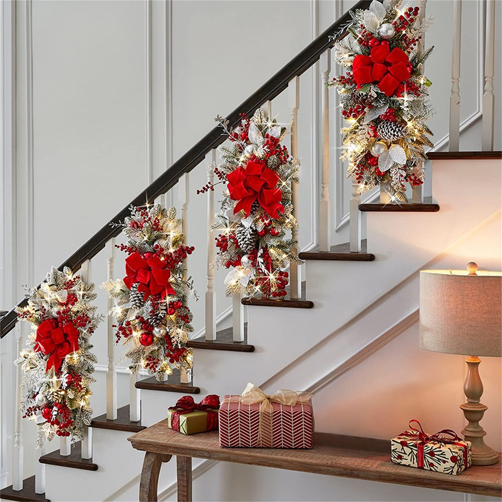 Eine Treppe, die für Weihnachten geschmückt ist. Rote Schleifen, Beeren und Lichter schmücken das Geländer. Geschenke stehen auf einem Tisch.