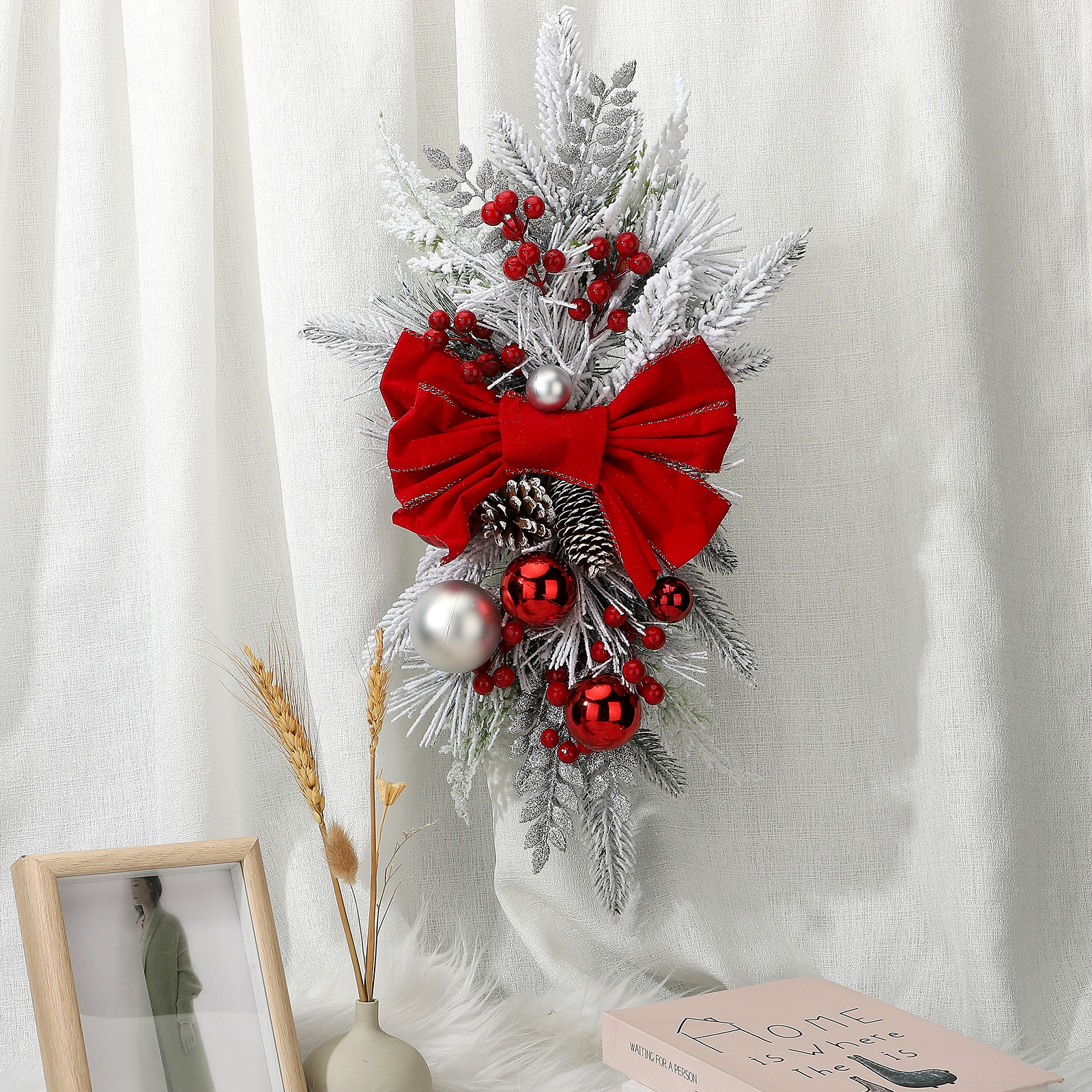 Eine Weihnachtsdekoration mit roter Schleife, Ornamenten und Beeren, hängt an einem weißen Vorhang.