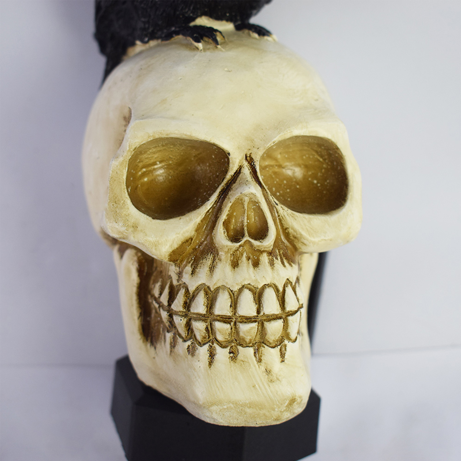 Eine Totenkopf-Figur mit einem schwarzen Vogel darauf. Der Schädel ist cremefarben mit detaillierten Zähnen.