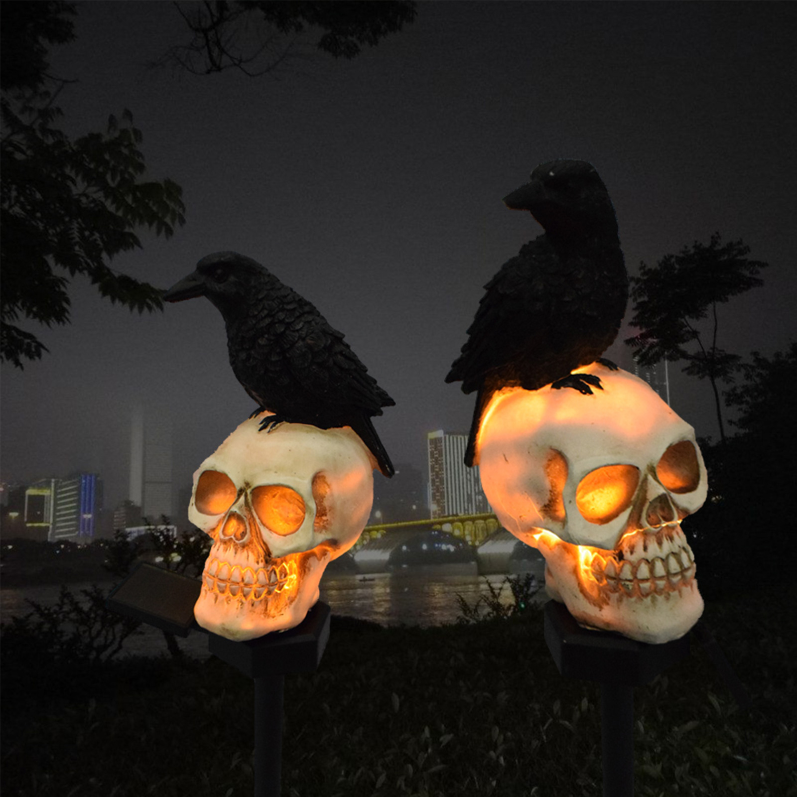 Zwei beleuchtete Totenkopfdekorationen mit schwarzen Raben. Nachtszene mit Brücke und Stadt im Hintergrund.