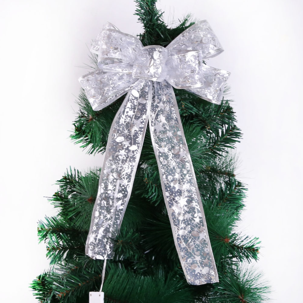 Eine Christbaumschleife aus silbernem Stoff mit Sternenmustern. Sie befindet sich auf einem grünen Weihnachtsbaum vor weißem Hintergrund.