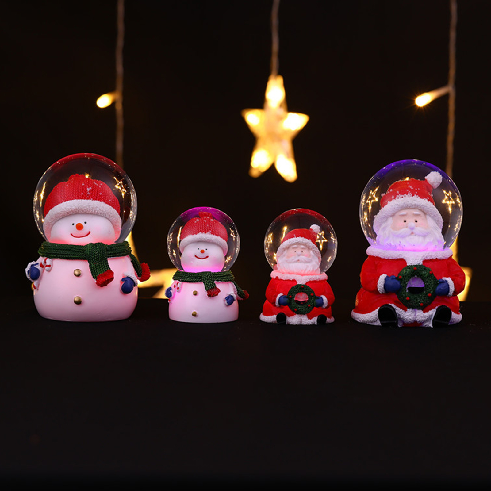 Vier Weihnachtsschmuckstücke: Schneemänner und Santa-Figuren in Schneekugeln. Lichter und Sterne im Hintergrund, schwarze Oberfläche.