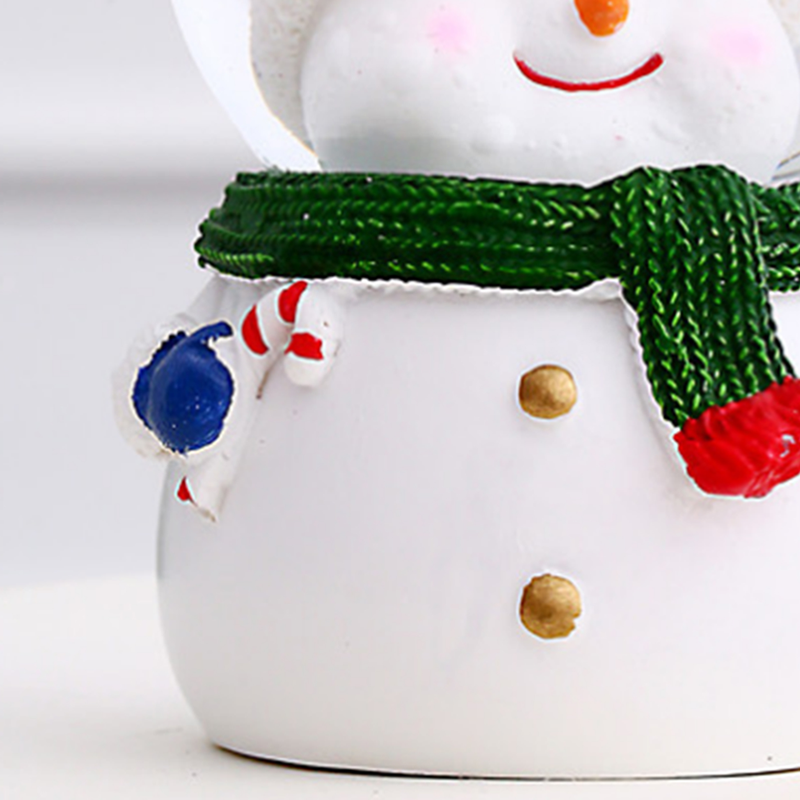 Eine Schneemannfigur mit grünem Schal, orangener Nase und rotem Lächeln, hält eine blaue Verzierung.