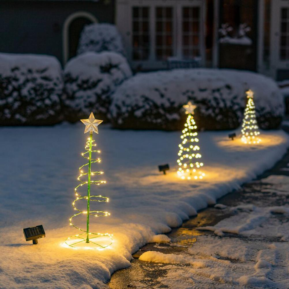 Beleuchtete Weihnachtsbäume im schneebedeckten Garten. Sterne oben drauf. Büsche und Haus im Hintergrund. Solar.