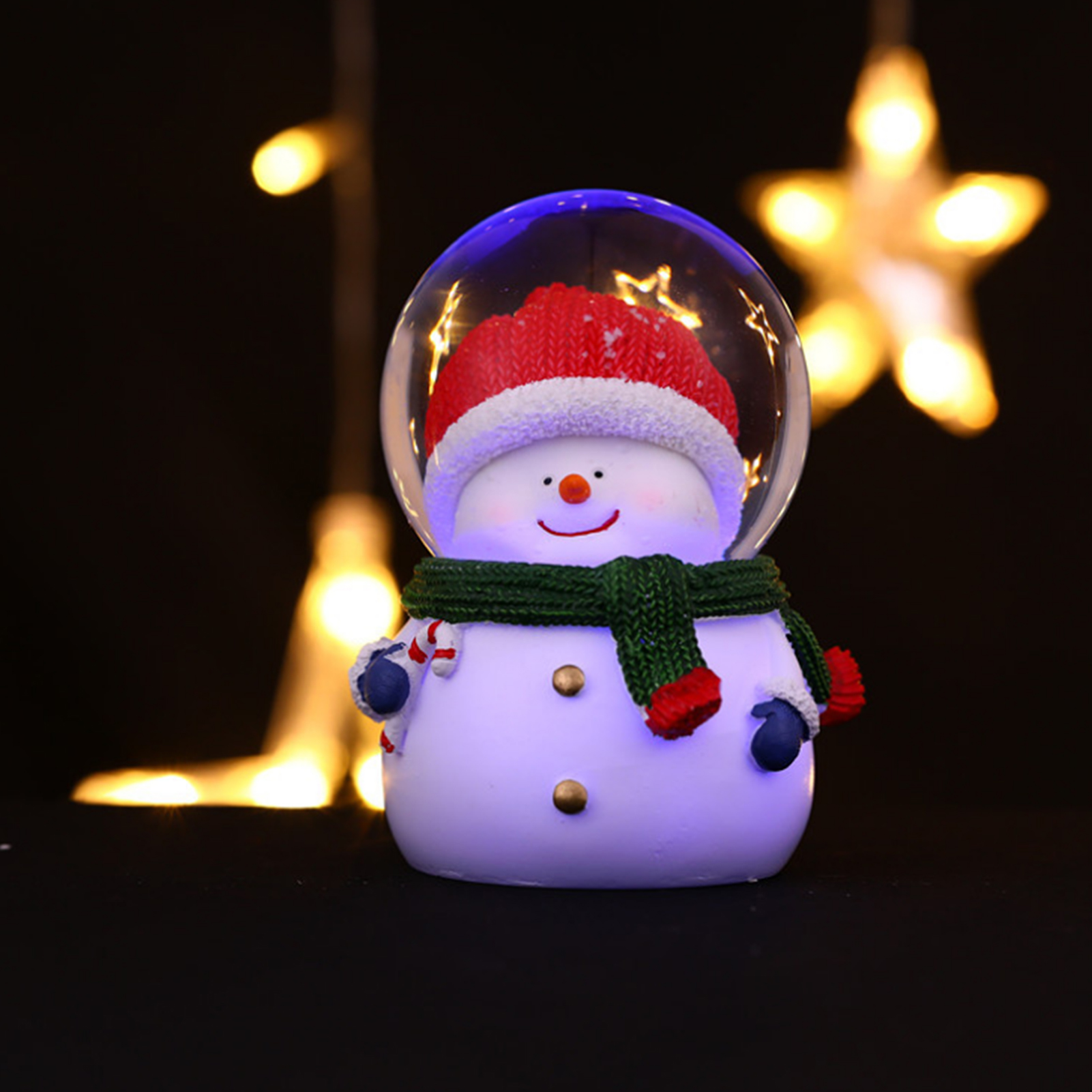 Eine Schneemannfigur mit roter Mütze und grünem Schal in einer Glaskugel, mit sternförmigen Lichtern im Hintergrund.