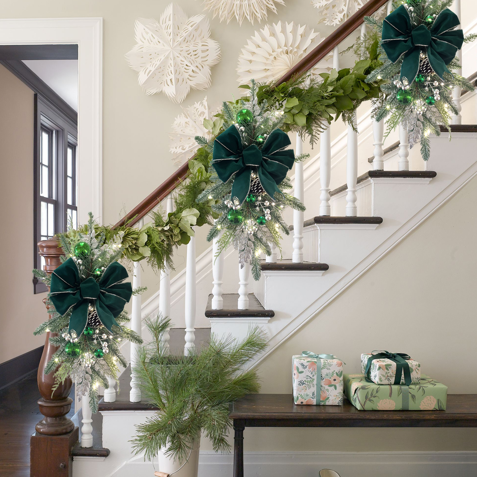Weihnachtlich dekorierte Treppe mit Girlande, Schleifen und Geschenken. Weiße Wände und Treppe, grüne und weiße Dekorationen.