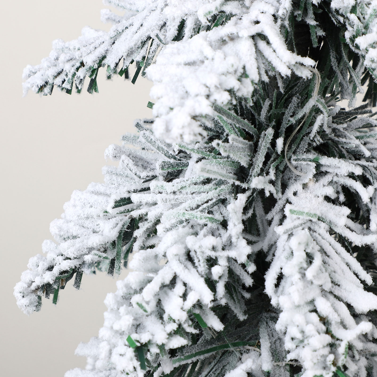 Nahaufnahme eines schneebedeckten Weihnachtsbaumzweigs. Die Nadeln sind grün und der Schnee ist weiß vor neutralem Hintergrund.