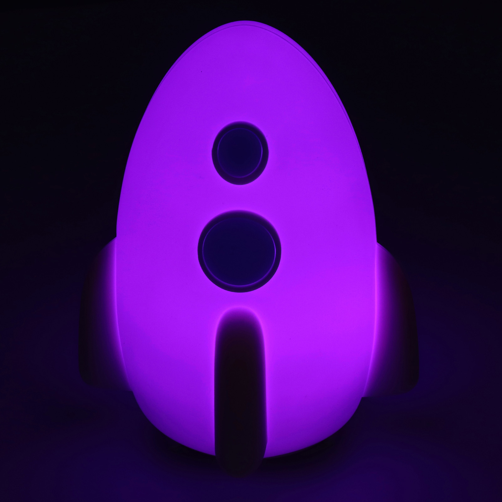 Eine lila raketenförmige Lampe mit zwei kreisförmigen Lichtern und zwei Flossen vor dunklem Hintergrund.