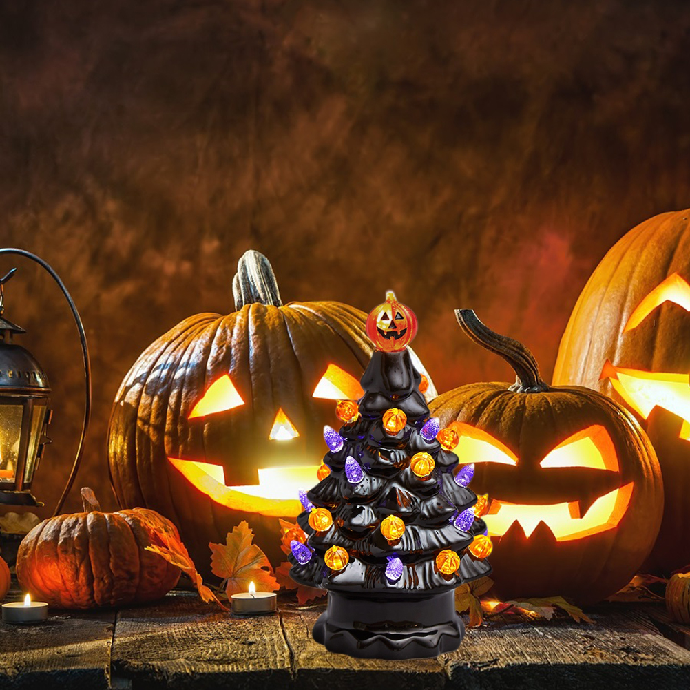 Ein schwarzer Keramik-Halloweenbaum mit Lichtern, umgeben von geschnitzten Kürbissen und Kerzen auf einer Holzoberfläche.