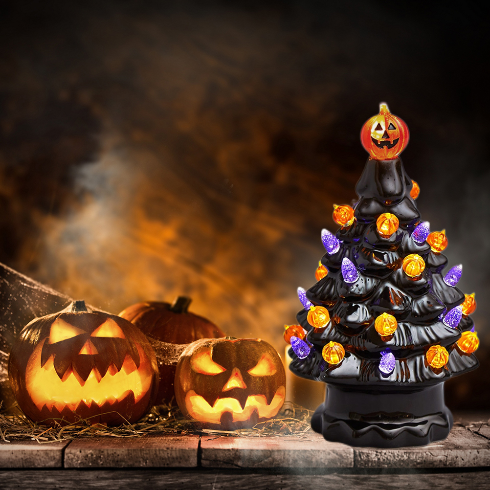 Eine Halloween-Szene mit einem schwarzen Keramikbaum mit orangefarbenen und lila Lichtern und drei geschnitzten Kürbissen.