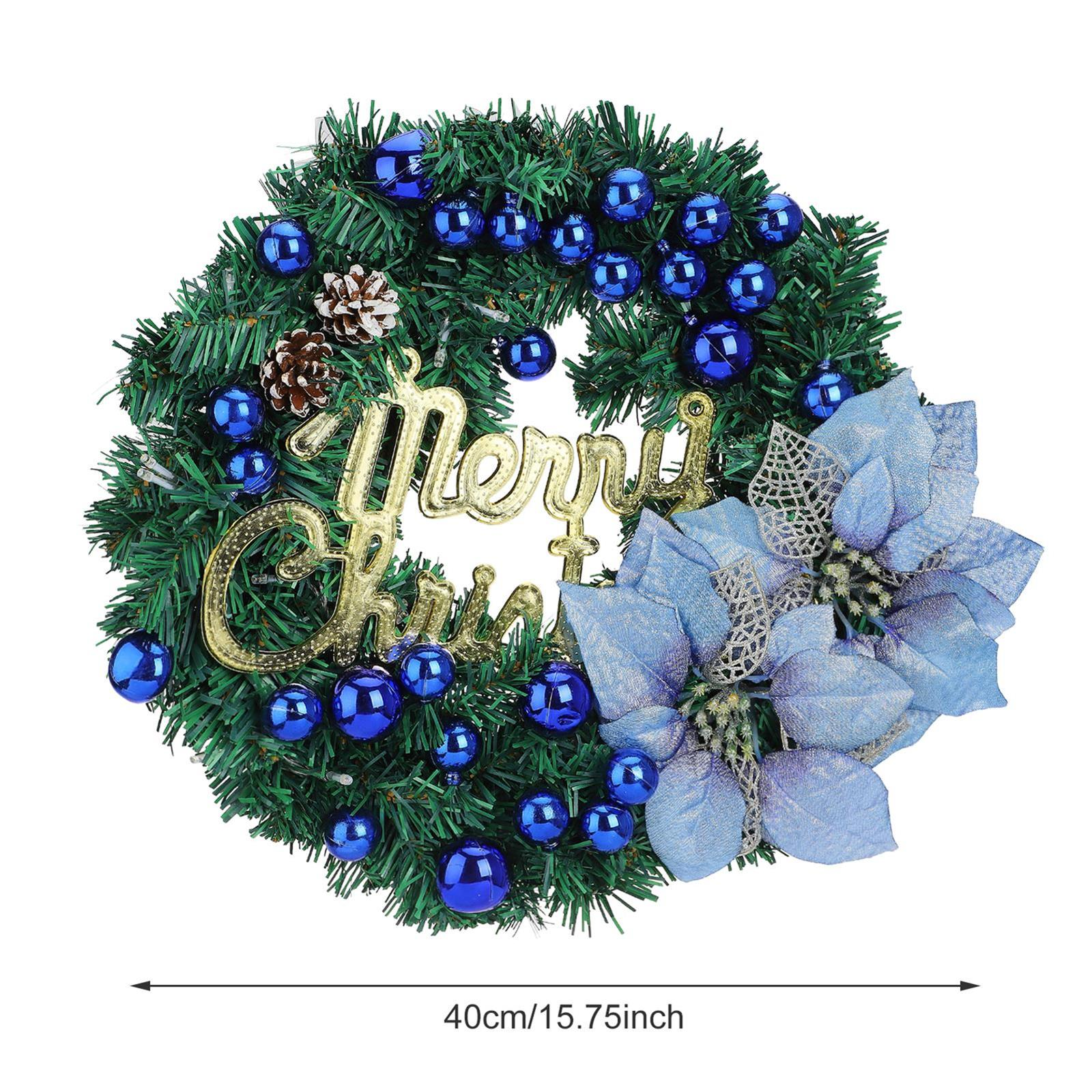 Ein Weihnachtskranz mit grünen Nadeln, blauen Ornamenten, Tannenzapfen, einem goldenen „Frohe Weihnachten“-Schild und blauer Blume.