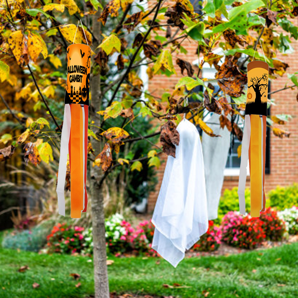Halloween-Dekorationen hängen an einem Baum: Windsocken und ein Geist. Herbstlaub und ein Backsteinhaus im Hintergrund.