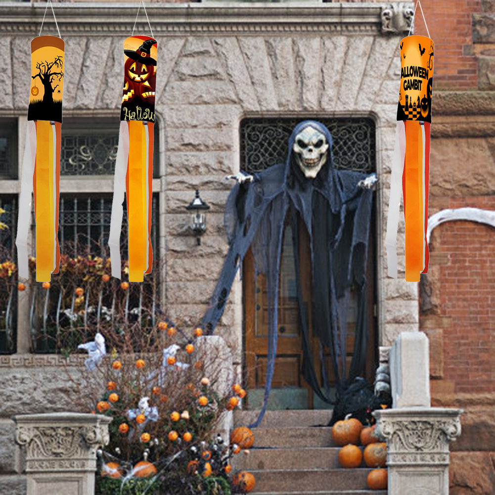 Halloween-Dekorationen. Windsäcke mit Kürbissen, ein gruseliges Skelett an der Tür, Kürbisse auf der Treppe und Büsche mit orangefarbener Dekoration.