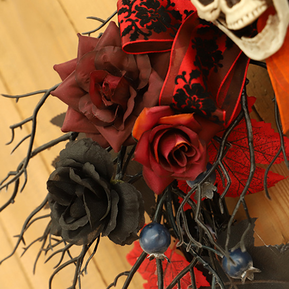 Ein Halloween-Kranz mit roten, weinroten und schwarzen Rosen, Beeren und einem Totenkopf. Rotes Band mit schwarzem Muster und dunklen Zweigen.
