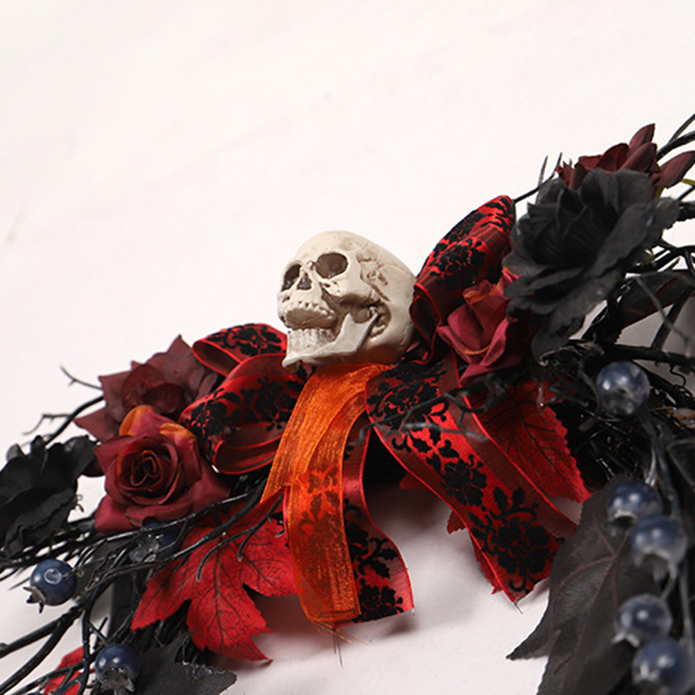 Ein Halloween-Kranz mit einem Totenkopf, roten Rosen, schwarzen Blumen, roten Blättern und blauen Beeren mit rotem Band.