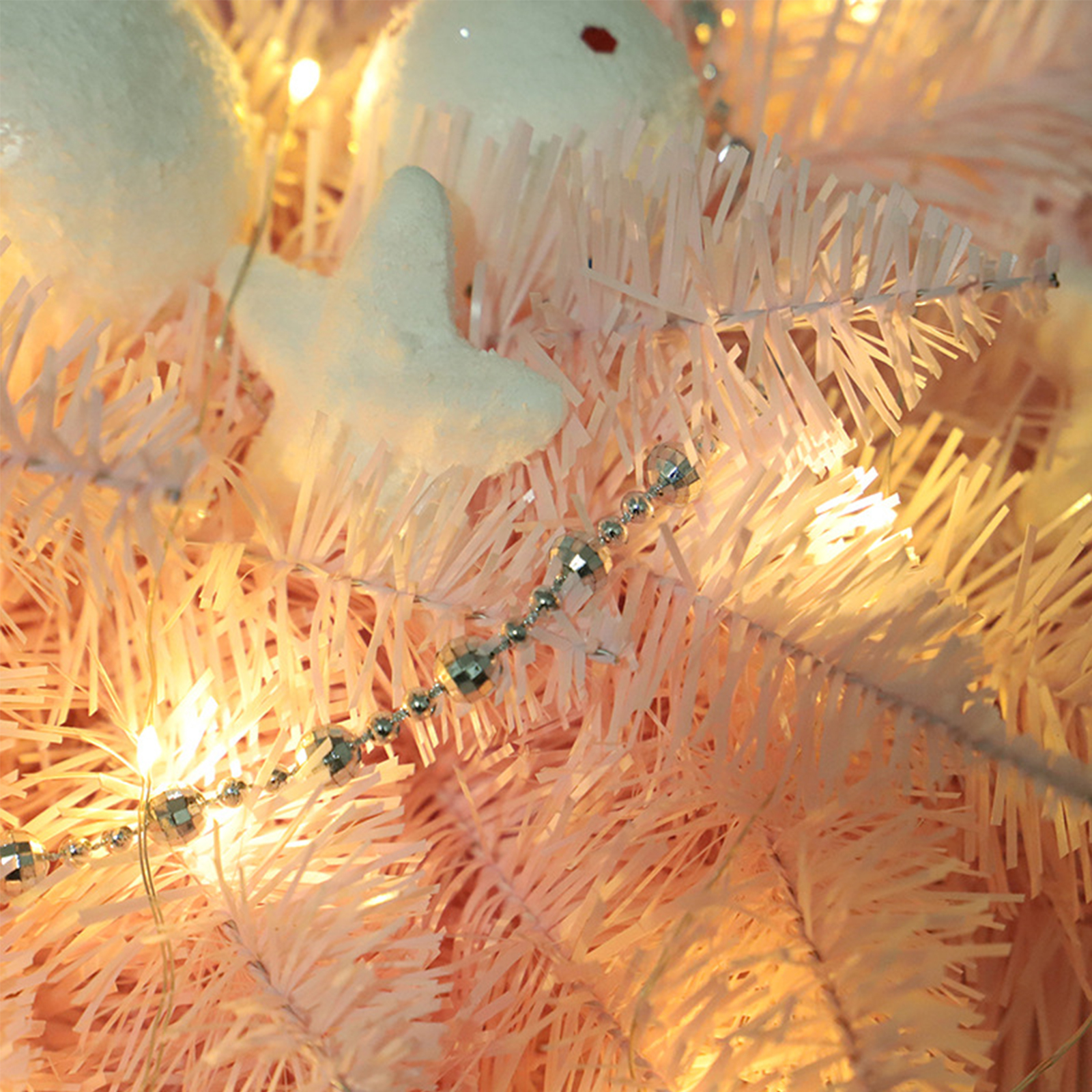 Nahaufnahme eines rosafarbenen Weihnachtsbaums, geschmückt mit weißen Sternornamenten und silberner Perlenkette. Warme Lichter scheinen.