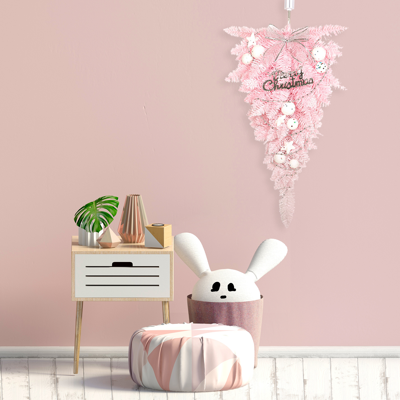 Ein pinkfarbener Weihnachtsbaum hängt an einer pinkfarbenen Wand. Darunter ein Beistelltisch mit Gegenständen und ein Hase im Korb.