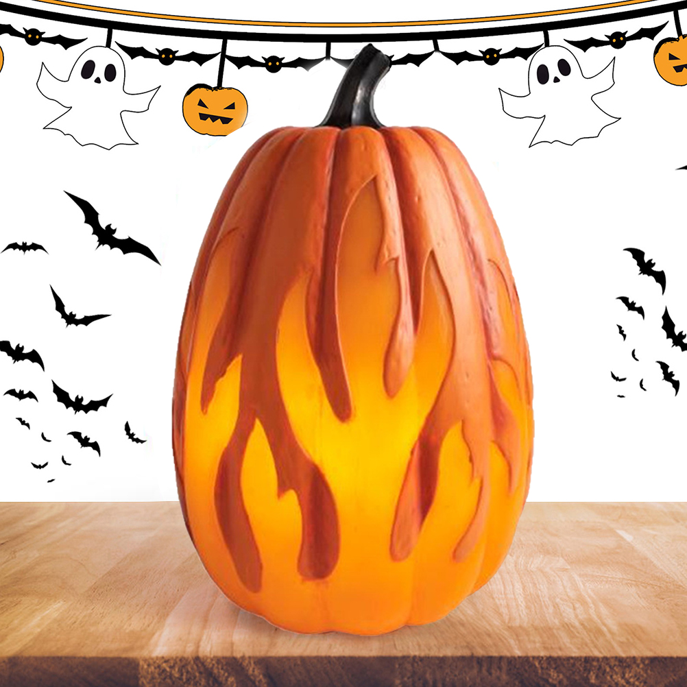 Ein beleuchteter orangefarbener Kürbis mit flammenartigen Ausschnitten steht auf Holz. Fledermäuse und Halloween-Dekorationen sind im Hintergrund.