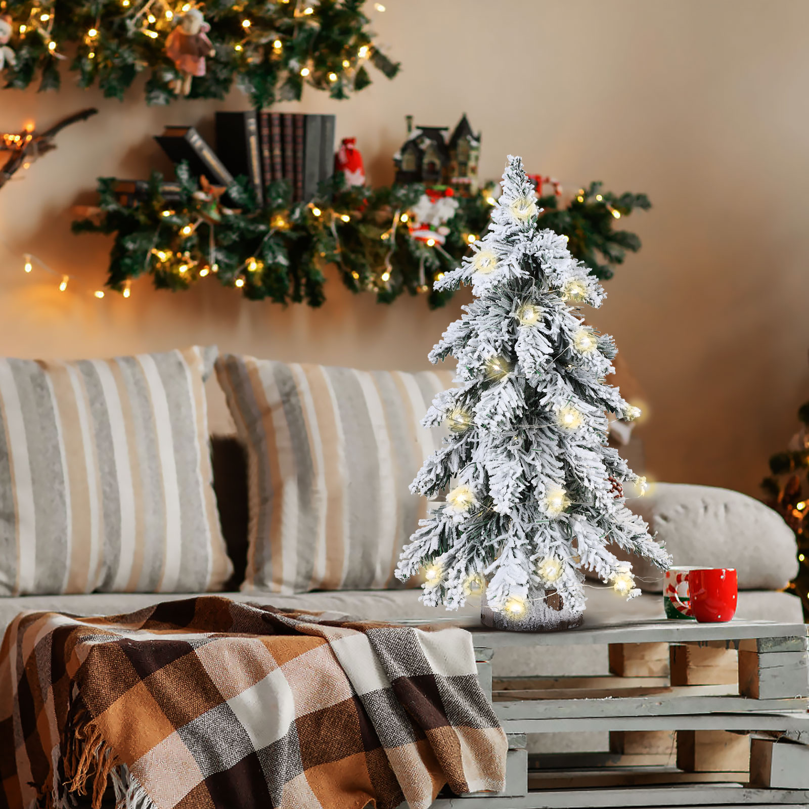 Ein dekorierter Weihnachtsbaum mit Lichtern auf einem Holztisch. Eine Decke und Kissen sind im Hintergrund.