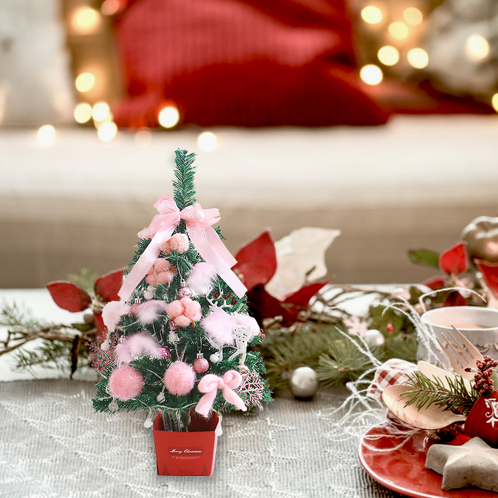 Ein kleiner Weihnachtsbaum mit rosa Dekorationen auf einem Tisch, der für die Feiertage gedeckt ist, mit Lichtern im Hintergrund.