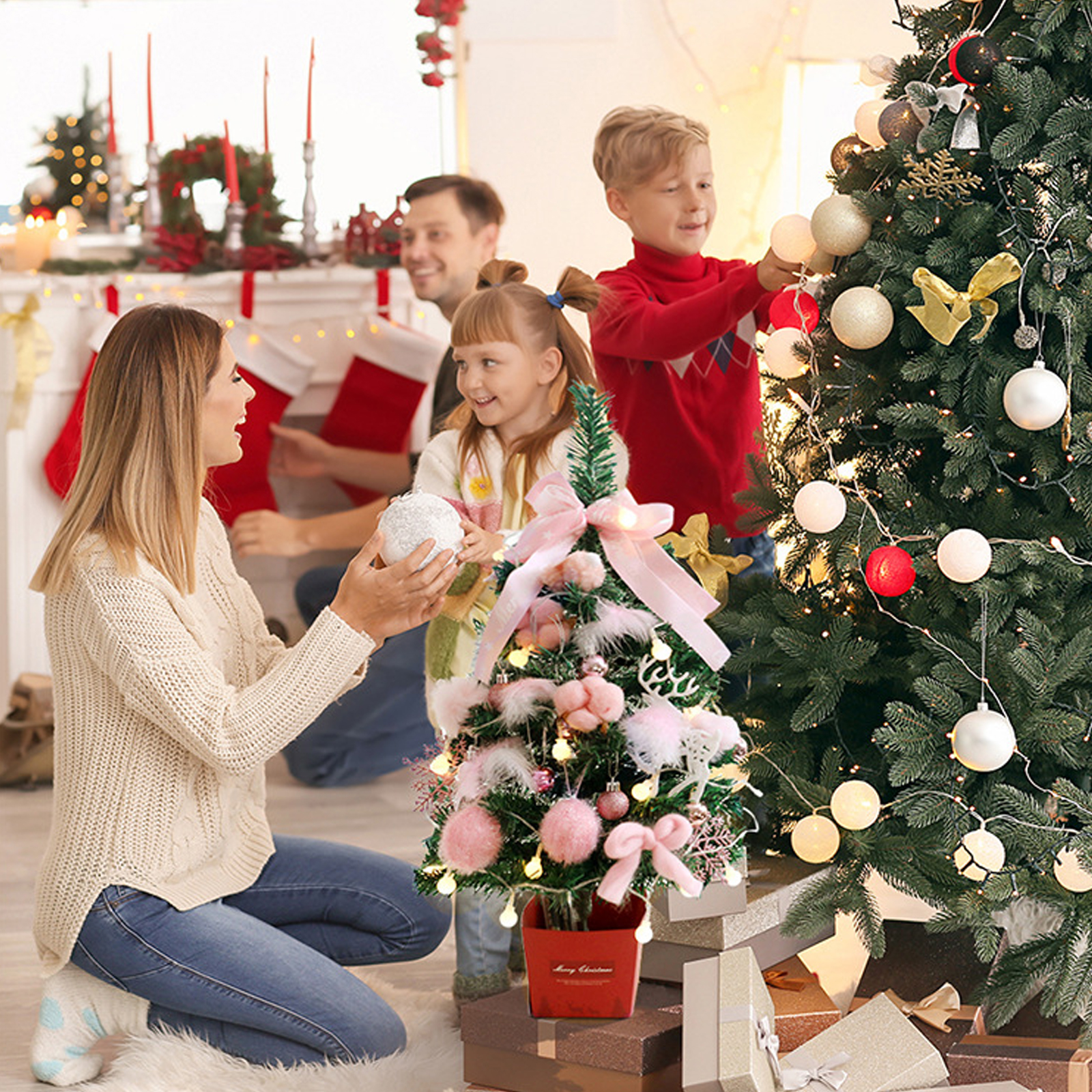 Familie schmückt Weihnachtsbäume. Frau kniet, hält Ornament. Junge und Mädchen dekorieren. Kamin im Hintergrund.