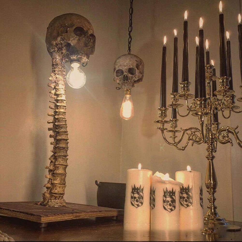 Ein Raum mit Dekorationen zum Thema Schädel. Eine Wirbelsäulenlampe, Schädel-Pendelleuchten, Kerzenhalter und Kerzen mit Schädelgrafiken sind sichtbar.