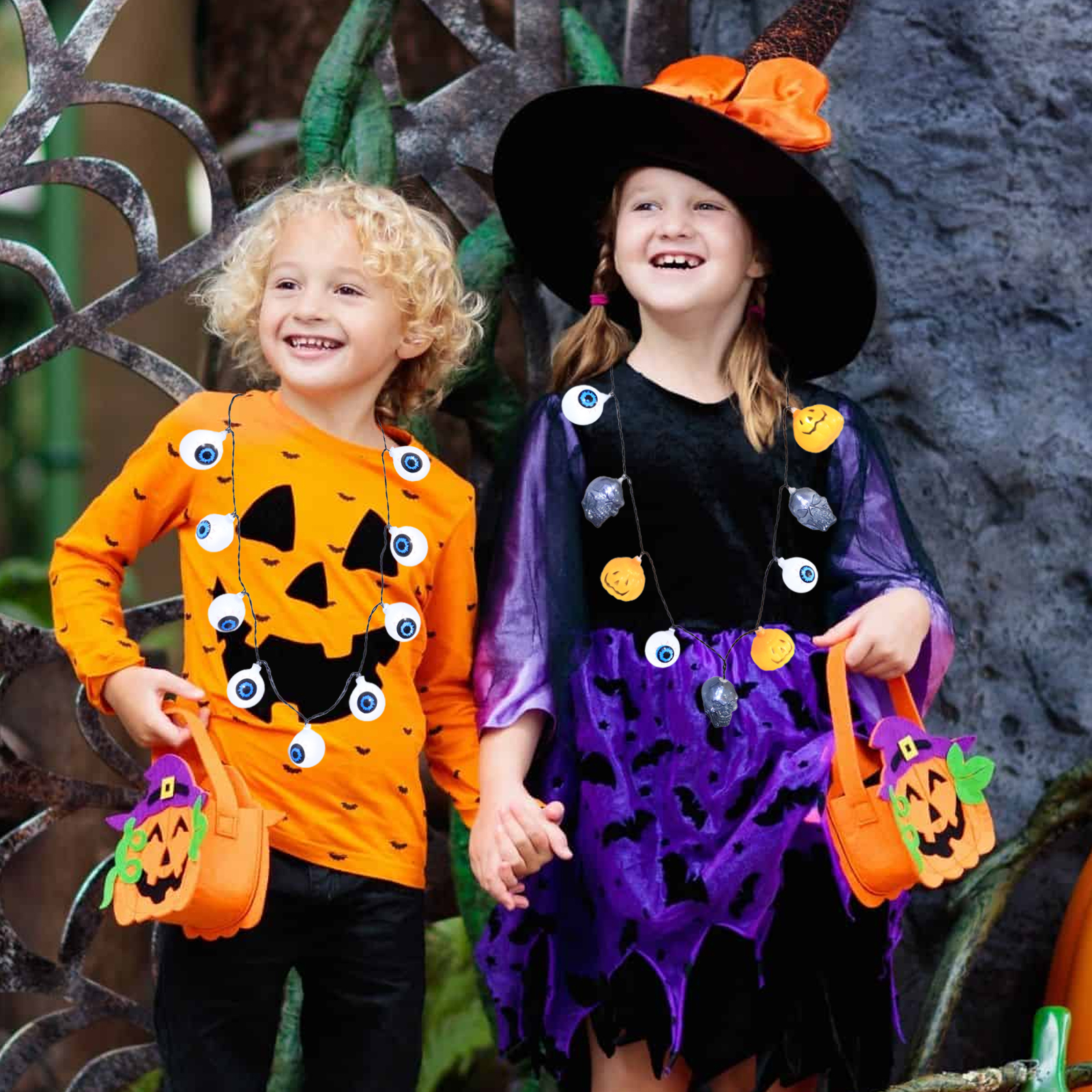 Zwei Kinder in Halloween-Kostümen, eines als Kürbis, das andere als Hexe, halten Süßigkeitentüten und lächeln.