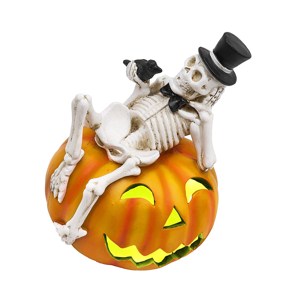 Ein Skelett mit Zylinder und Fliege liegt auf einem orangefarbenen Kürbis mit leuchtendem Gesicht. Ein schwarzer Vogel sitzt auf der Hand des Skeletts.