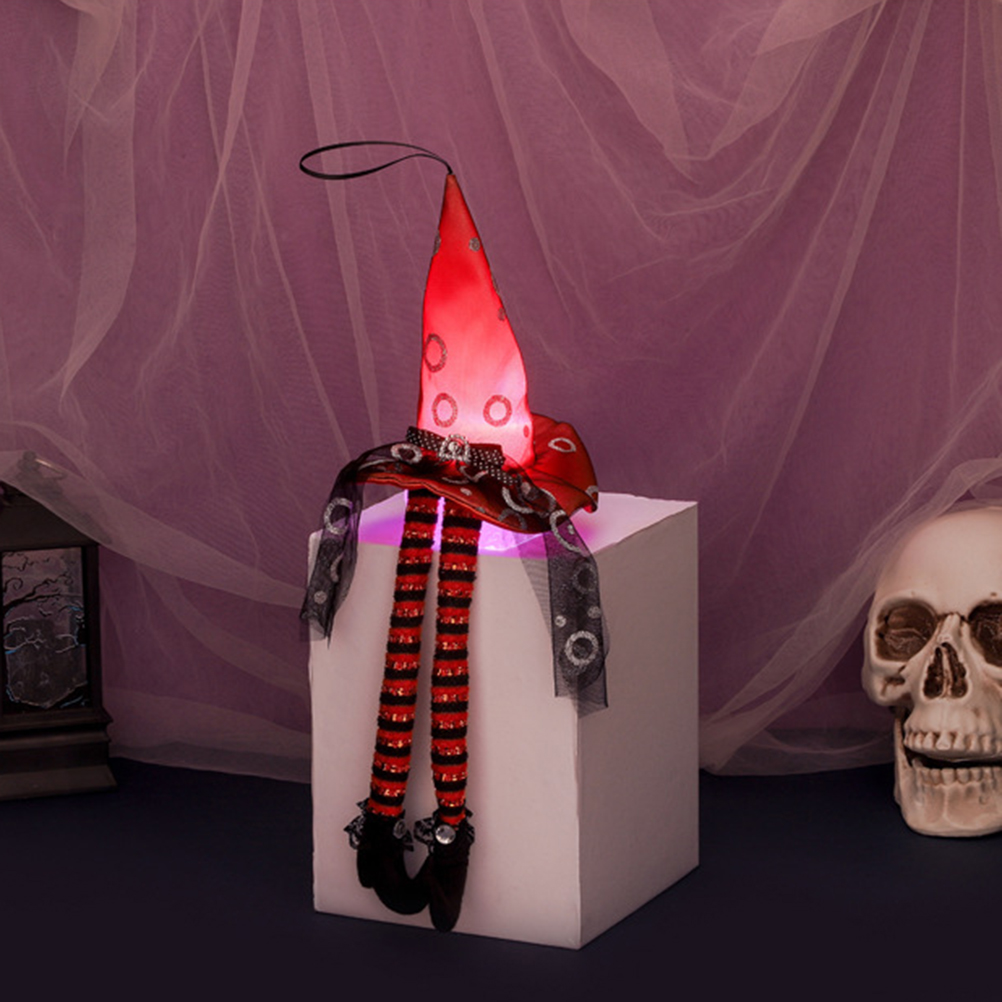 Eine Halloween-Dekoration: ein Hexenhut mit Beinen auf einem weißen Würfel. Ein Totenkopf und eine Laterne sind im Hintergrund.