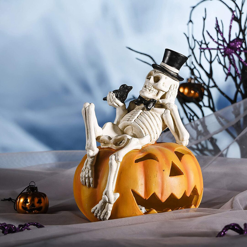 Ein Skelett mit Zylinder und Fliege sitzt auf einem geschnitzten Kürbis und hält einen schwarzen Vogel. Halloween-Dekoration.