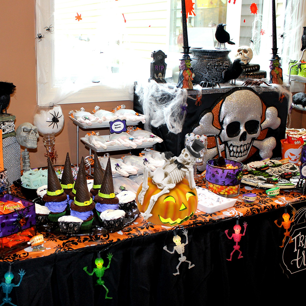 Ein Halloween-Tisch mit Cupcakes, einem Totenkopf, einem Kürbis mit Skelett und anderen thematischen Gegenständen.