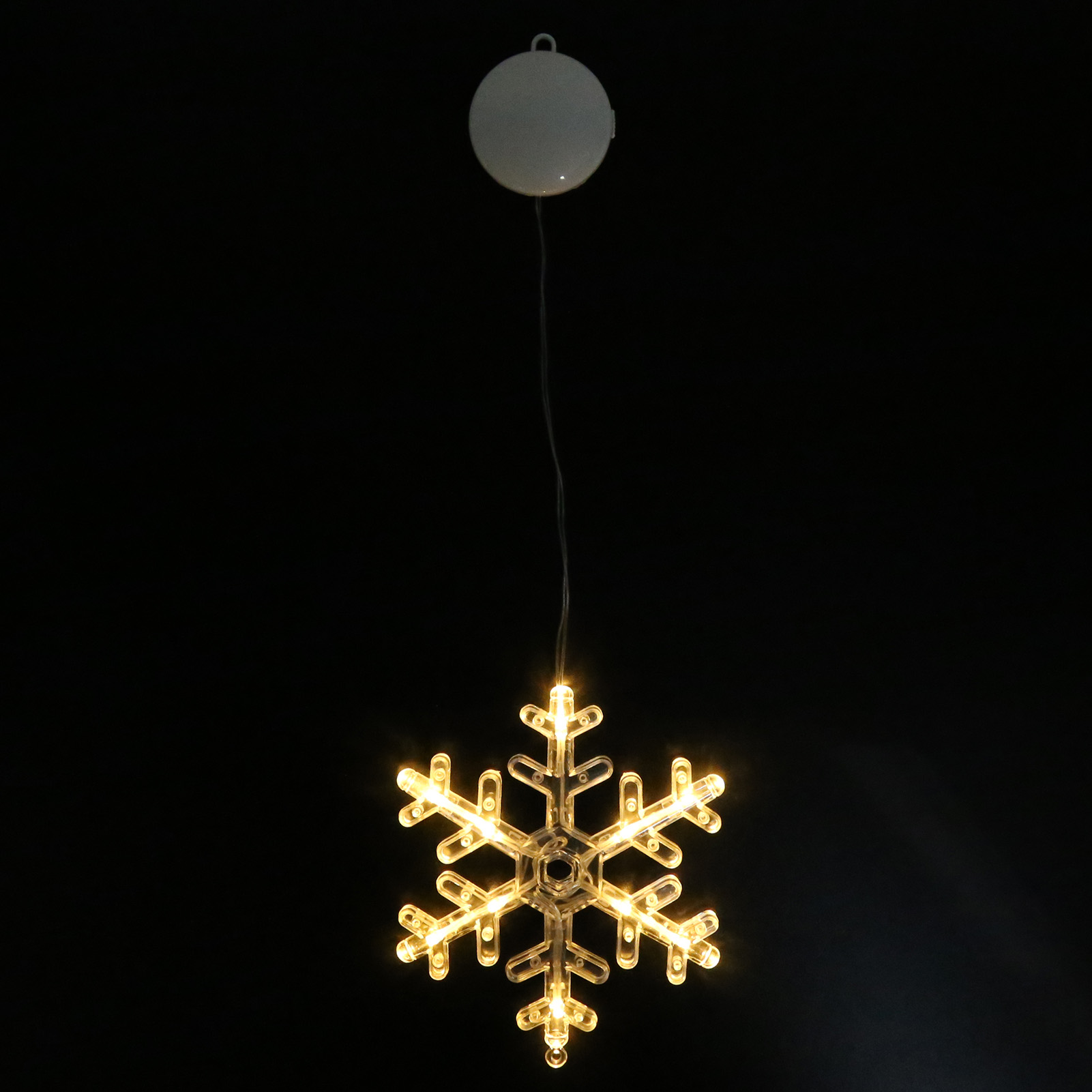 Eine leuchtende Schneeflocken-Weihnachtsdekoration hängt vor einem schwarzen Hintergrund. Sie hat gelbe Lichter und hängt an einem Draht.