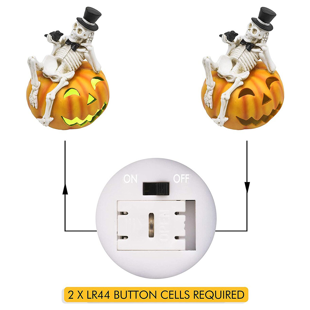 Zwei Skelette mit Zylinder sitzen auf geschnitzten Kürbissen. Darunter befindet sich ein Batteriefach und der Text "2 X LR44 BUTTON CELLS REQUIRED".