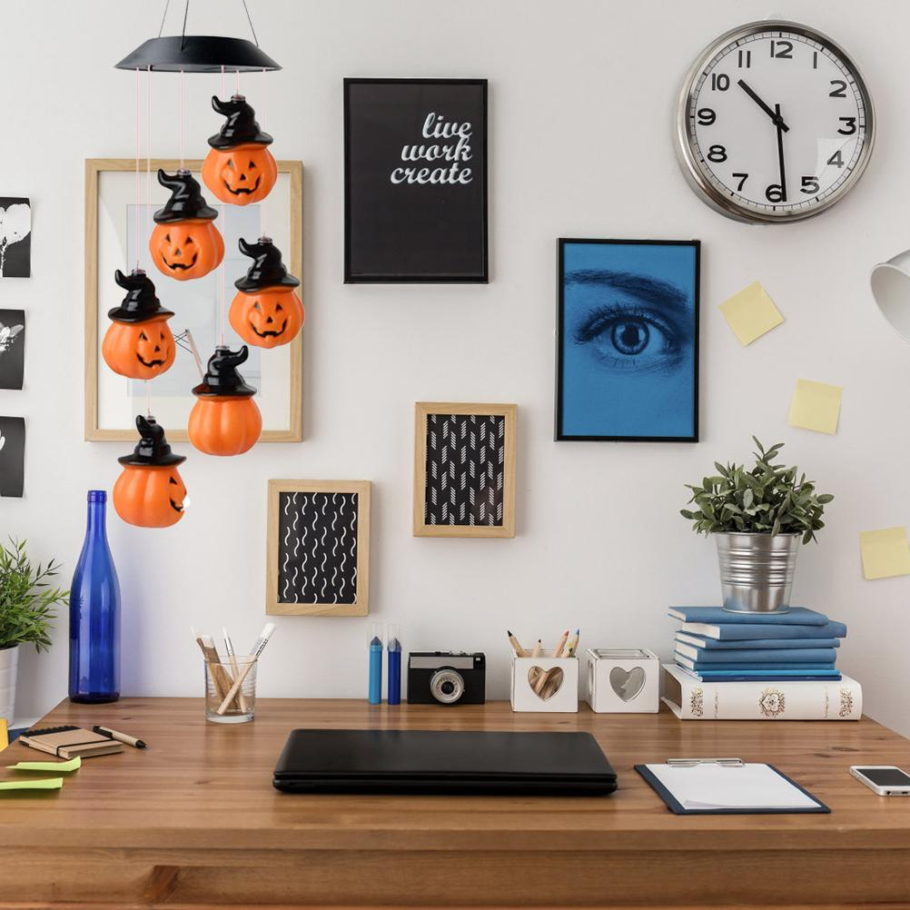 Ein Schreibtisch mit Halloween-Dekorationen, darunter Kürbislichter. Es gibt eine Uhr, gerahmte Kunst und einen Laptop.