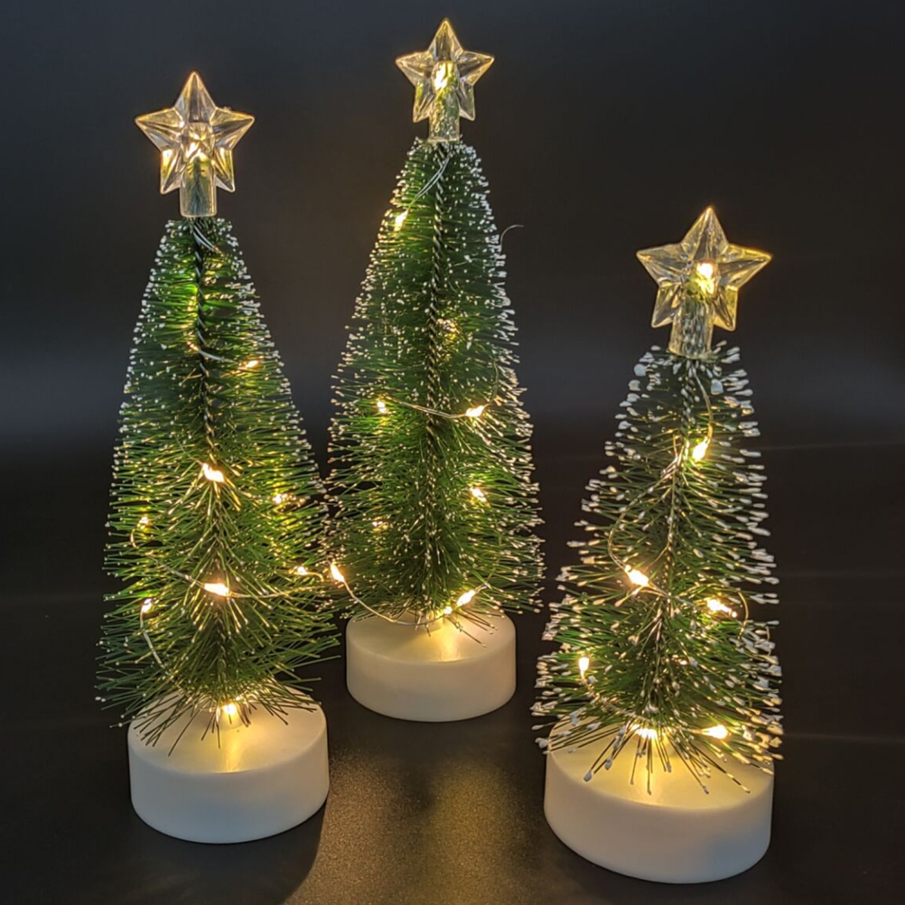 Drei kleine Weihnachtsbäume mit Sternaufsätzen und Lichterketten. Weiße Sockel und grüne Nadeln. Schwarzer Hintergrund.