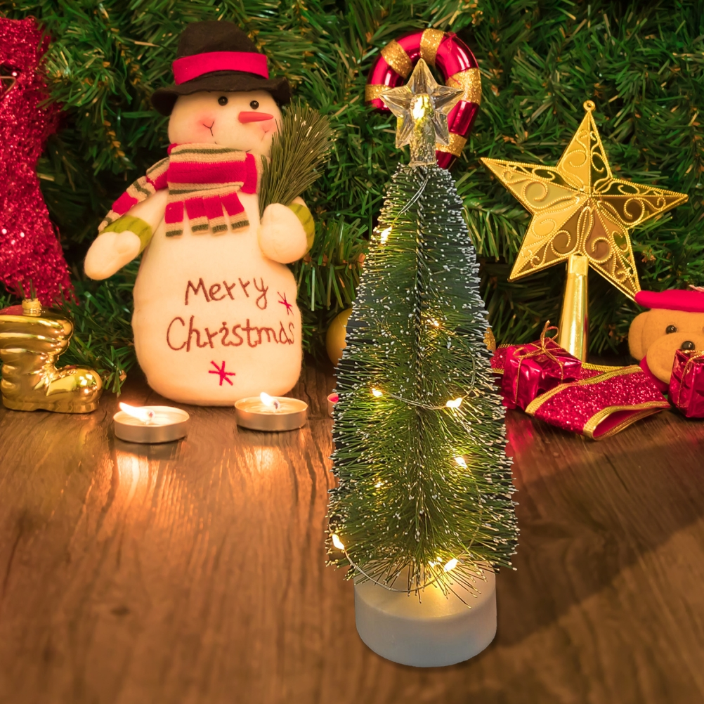 Eine Weihnachtsszene mit einem Schneemann, einem kleinen Baum mit Lichtern, Kerzen und Dekorationen auf einer Holzoberfläche.