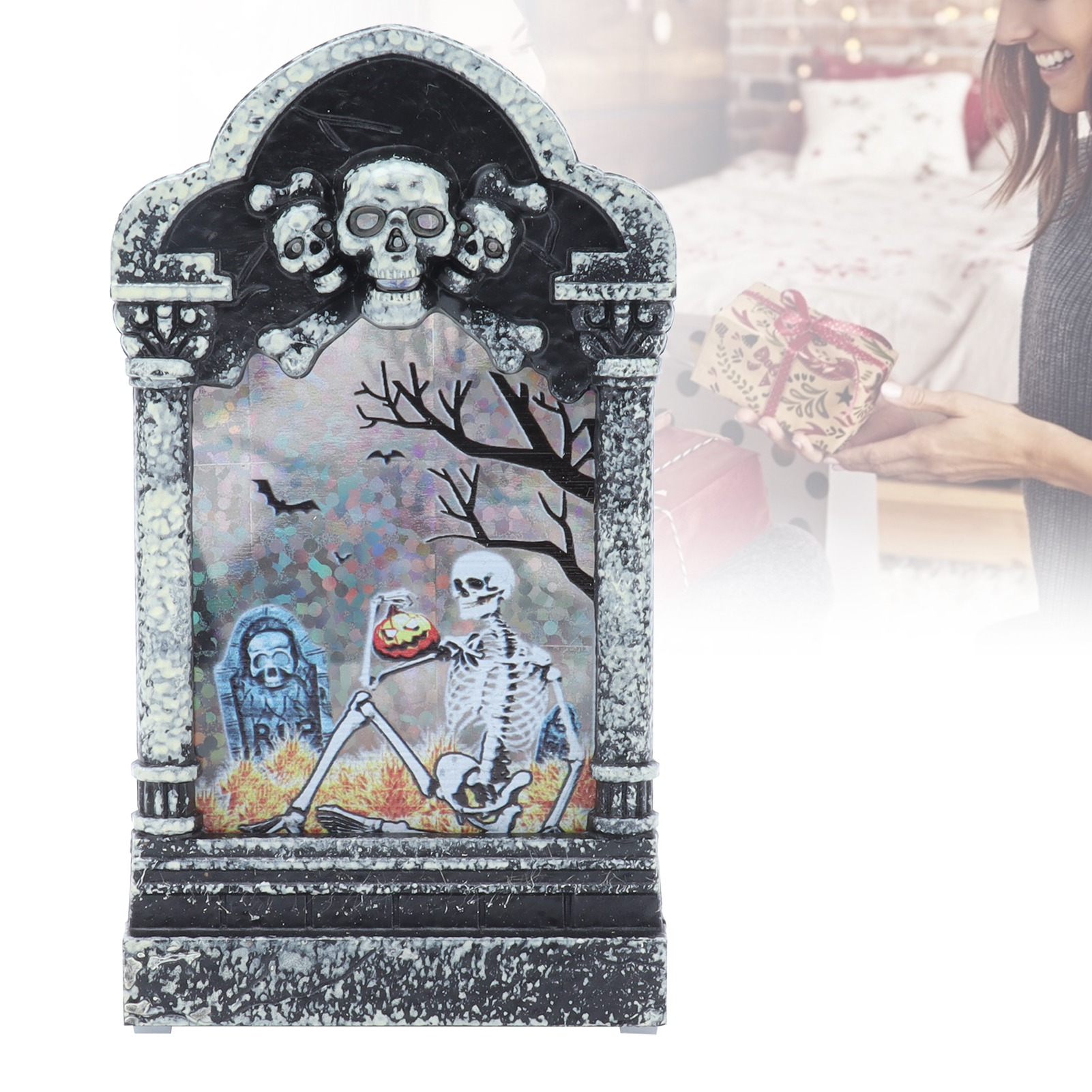 Halloween-Grabstein mit Totenkopf, Skelett mit Kürbis und eine Frau, die im Hintergrund eine Geschenkbox hält.