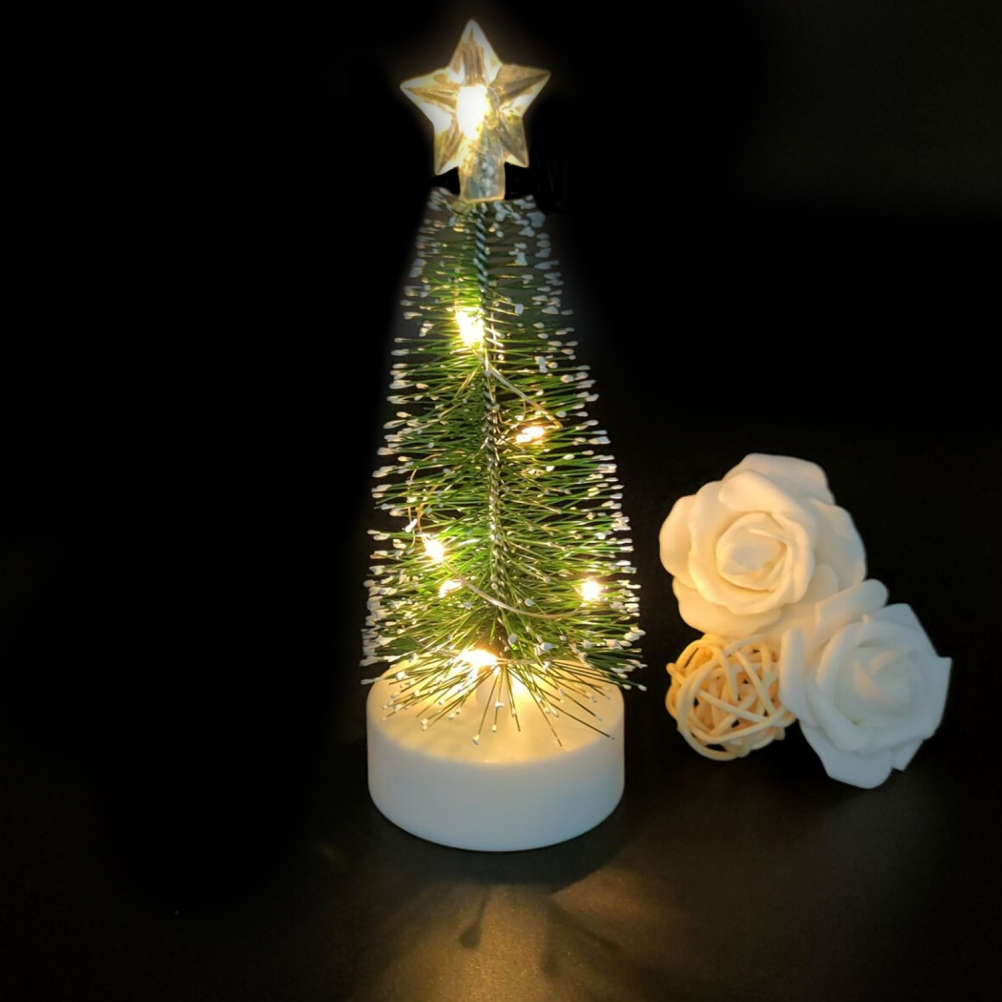 Ein kleiner Weihnachtsbaum mit Lichtern und einem Stern, mit weißen Rosen und einem Ball auf schwarzem Hintergrund.