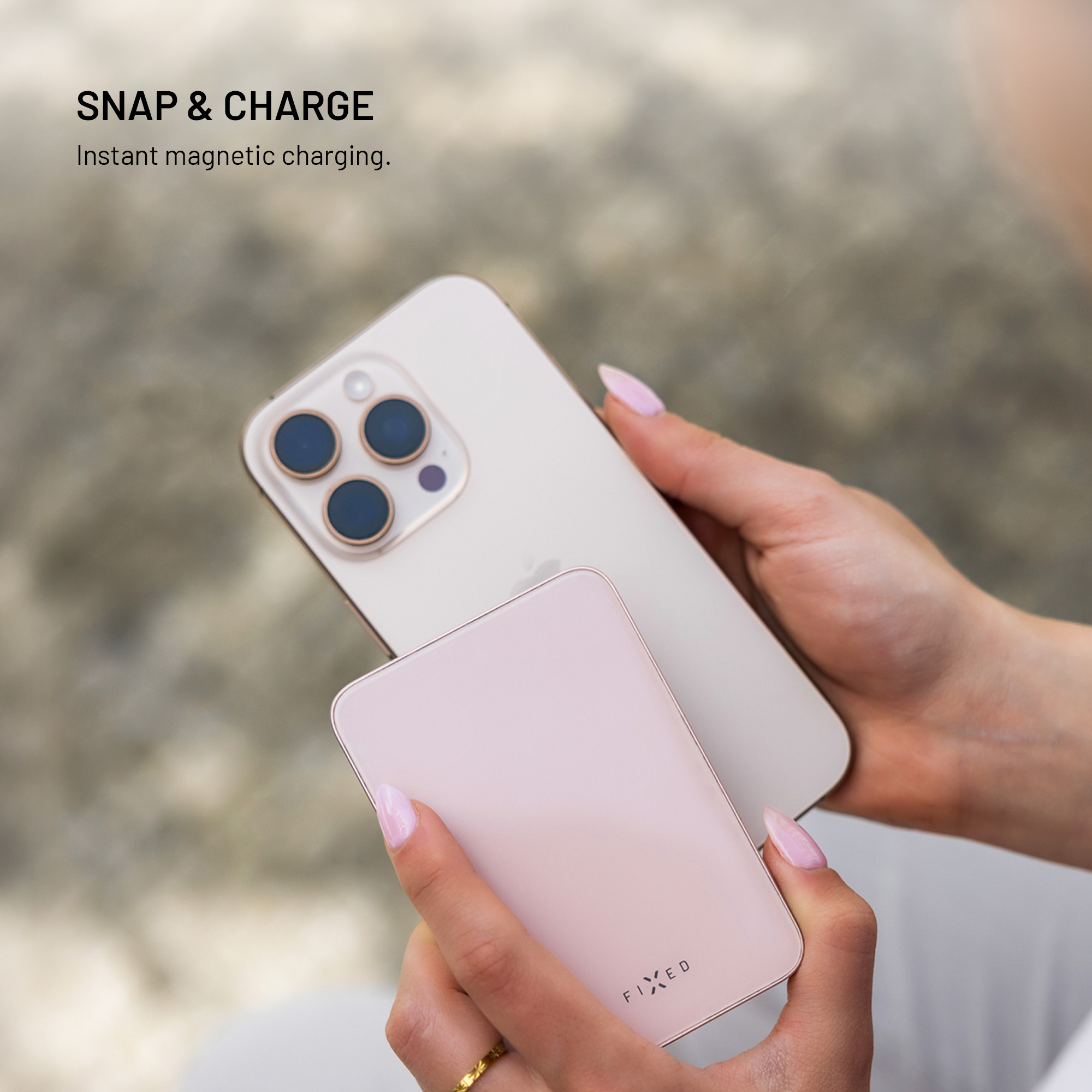 Hände halten ein weißes iPhone und eine rosa Powerbank. Das Telefon hat blaue Kameralinsen. Der Hintergrund ist verschwommen.