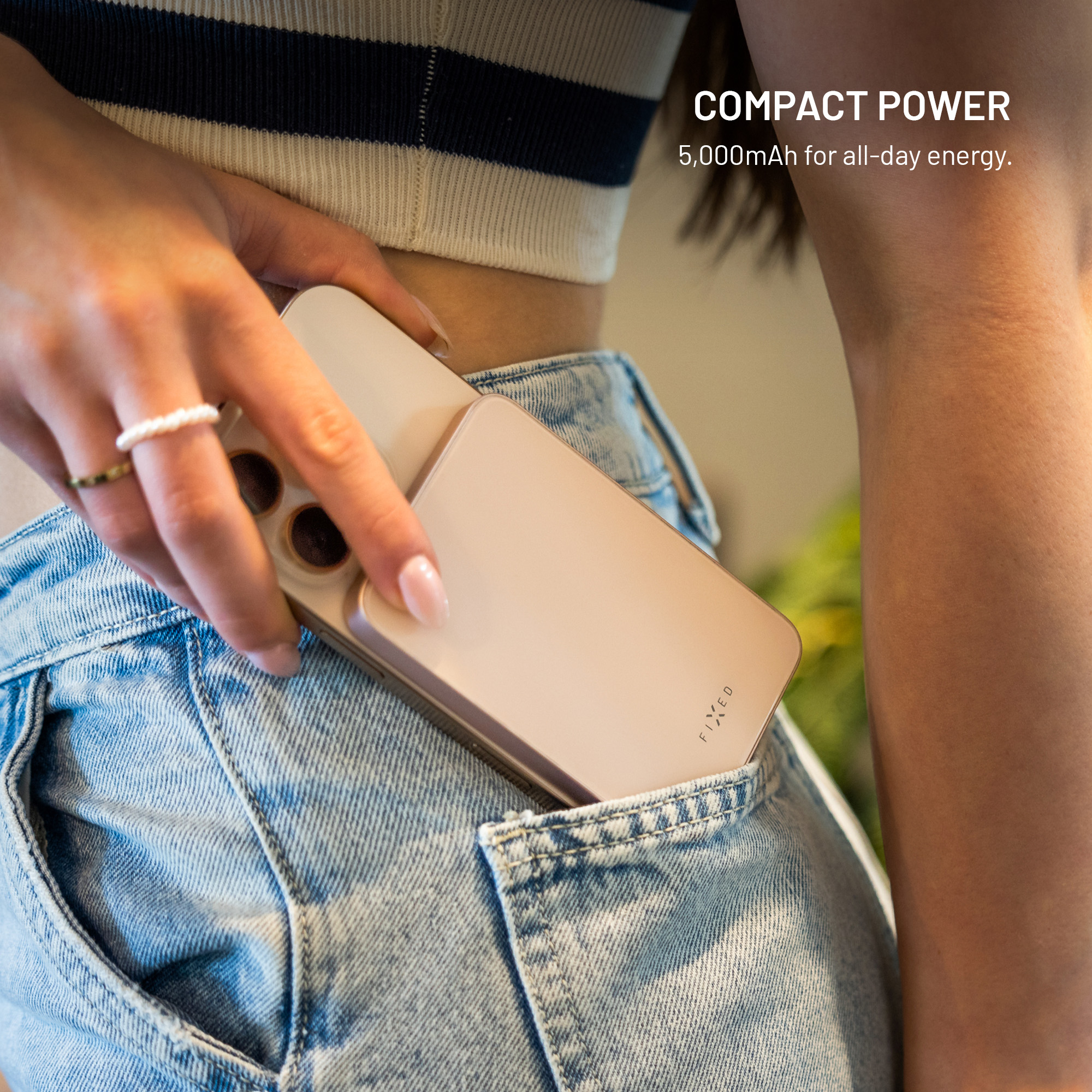 Eine Frau in Jeans hält ein Telefon in ihrer Tasche. Das Telefon ist goldfarben und der Text auf dem Bild lautet "COMPACT POWER".