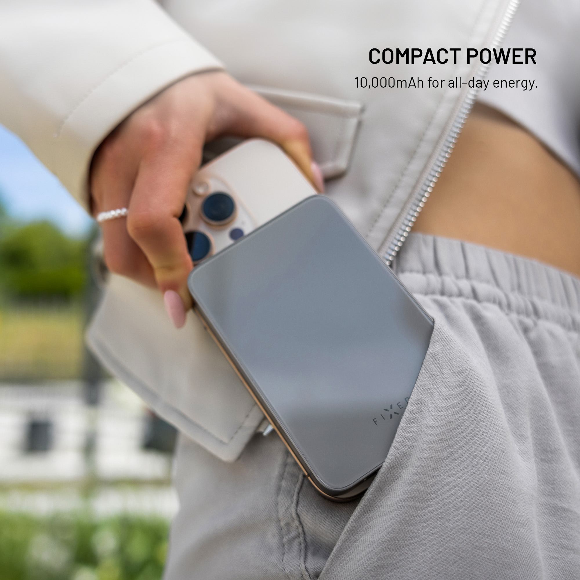 Eine Person hält ein Telefon und eine graue Powerbank. Die Powerbank befindet sich in der Tasche. Text: Kompakte Leistung, 10.000 mAh für den ganzen Tag.