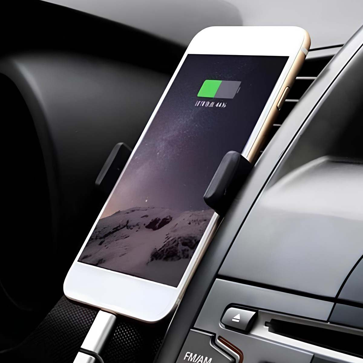 Smartphone in carica in auto. Il telefono mostra una scena di montagna e la batteria al 44%. È tenuto da un morsetto nero.