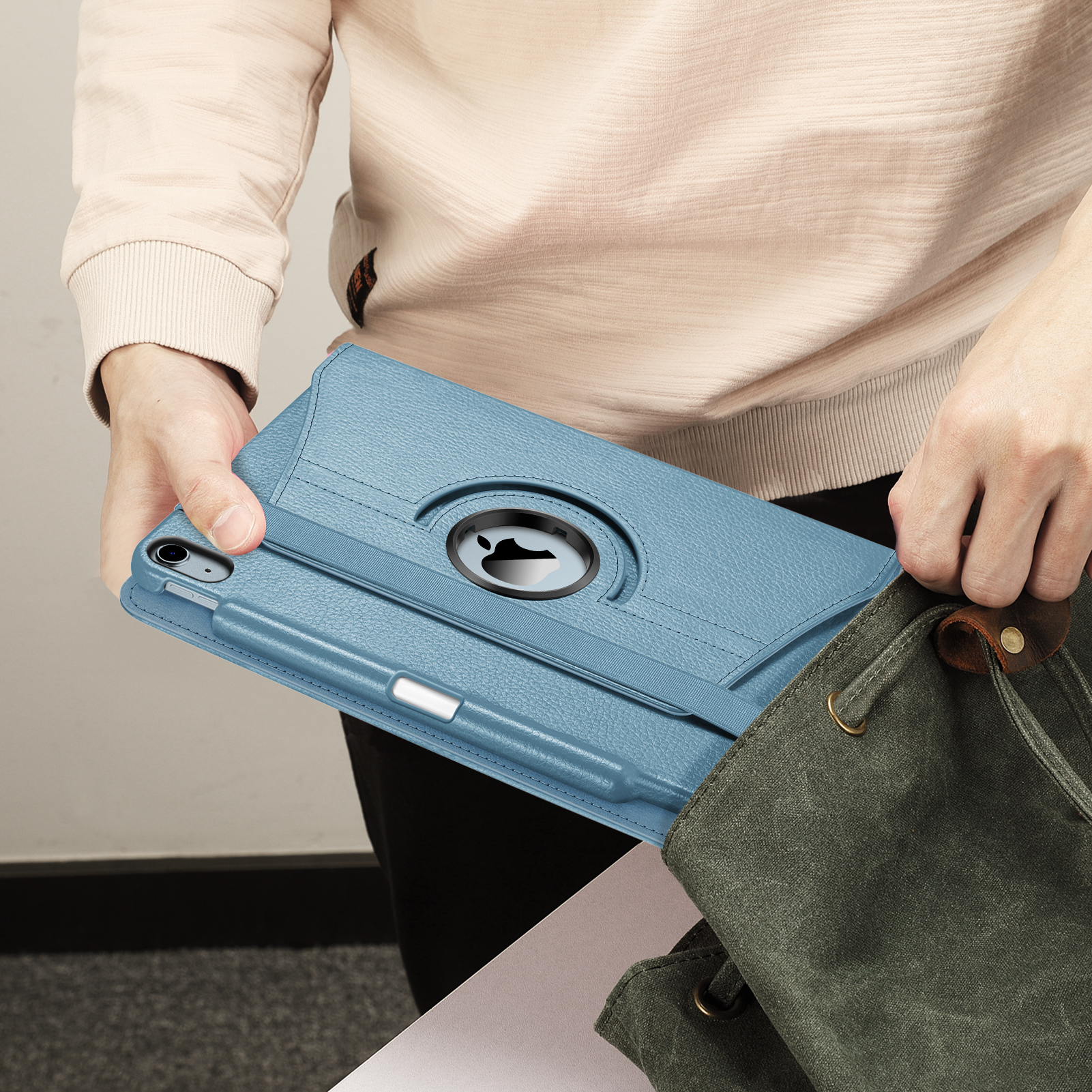 Eine Person, die eine hellblaue Tablethülle mit einem Stift hält und sie in eine grüne Canvas-Tasche legt.