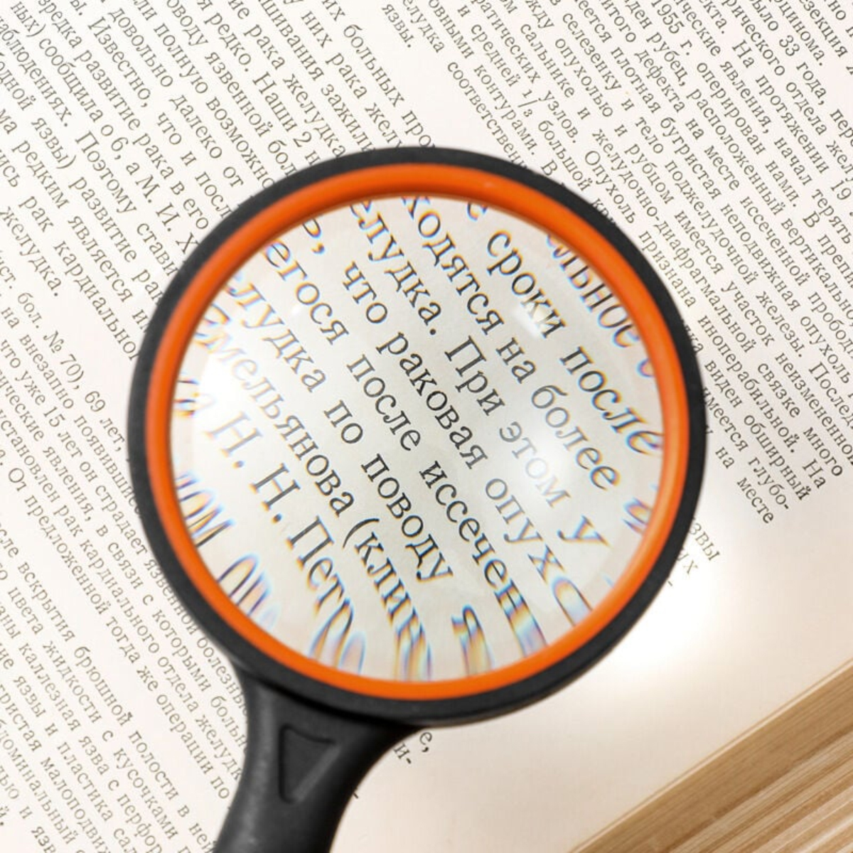 Eine Lupe mit orangefarbenem Rand liegt über einem Buch. Der Text ist auf Russisch. Das Glas vergrößert den Text.