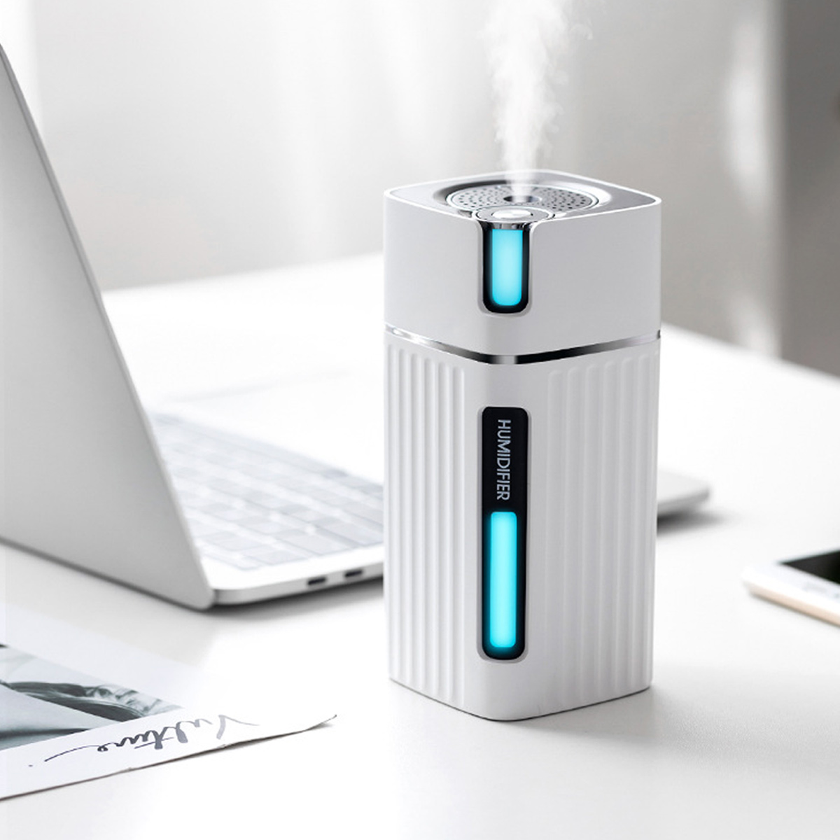 Weißer Luftbefeuchter mit Laptop im Hintergrund. Er hat ein blaues Licht und gibt Dampf ab. Das Wort HUMIDIFIER ist sichtbar.